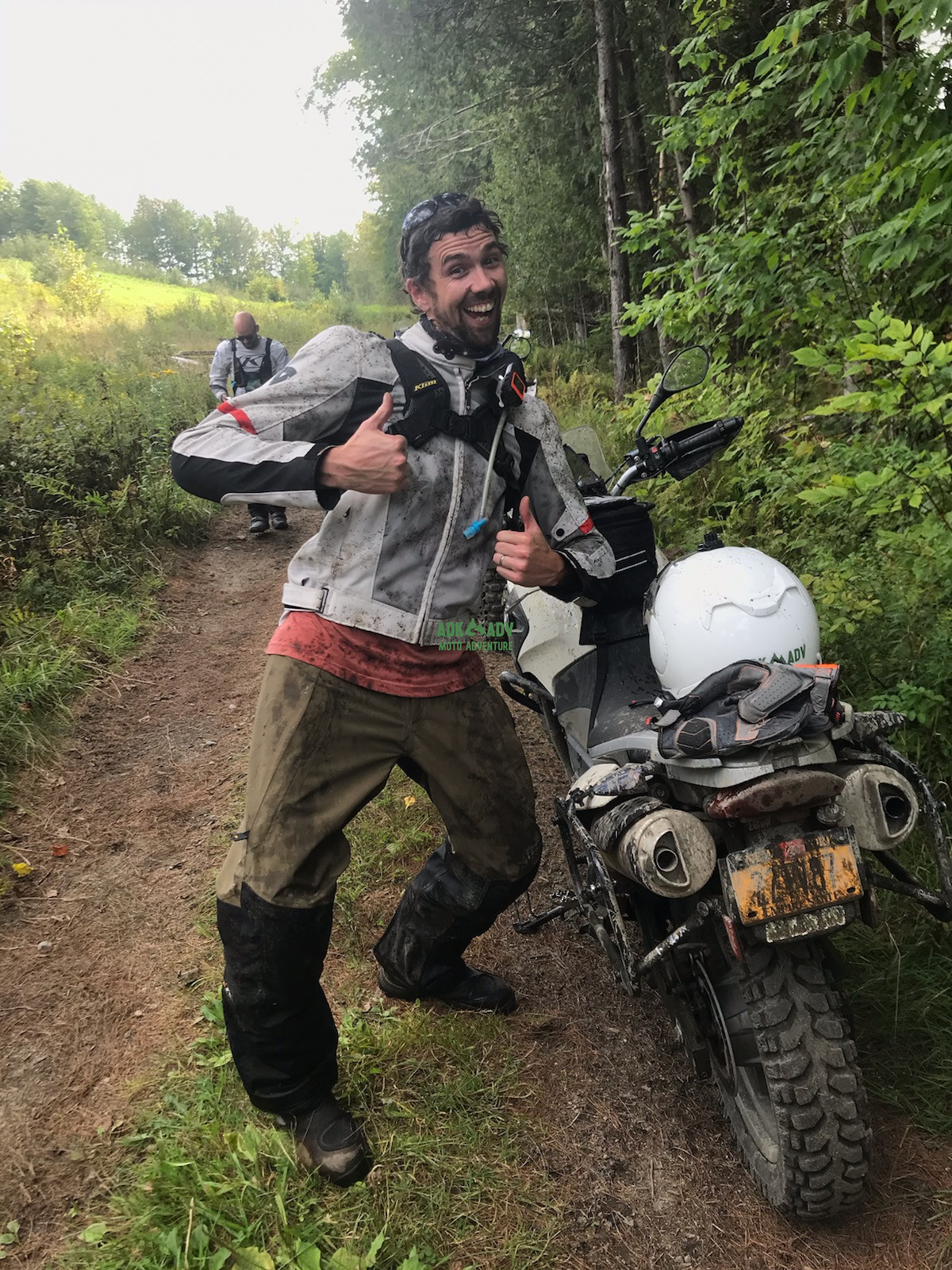img-20230912-201929.jpg {A man in motorcycle gear stands next to a an offroad motorcycle. They are both on a wooded trail and covered in mud. The man is smiling.}